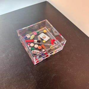 Puede incluir: Un plato cuadrado de plástico transparente con un diseño colorido y moteado. El plato está lleno de varias píldoras y cápsulas de colores.