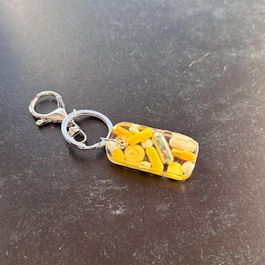 May include: A yellow and clear resin keychain with a silver key ring. The resin contains small yellow and white pills and sprinkles.