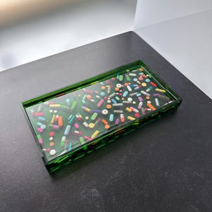Könnte beinhalten: Ein grünes rechteckiges Tablett gefüllt mit bunten Kapseln. Das Tablett besteht aus klarem Harz mit einem grünen Rand.