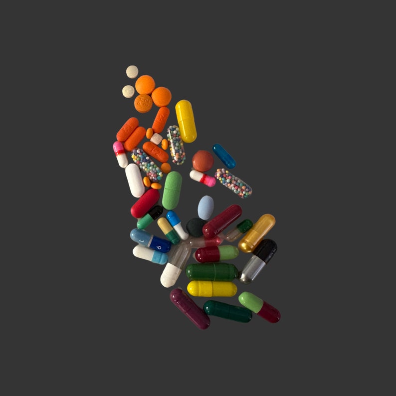 May include: Assortment of colorful pills and capsules, including orange tablets, yellow capsules, and red and white capsules, against a dark gray background. The pills vary in size and shape, suggesting different medications.