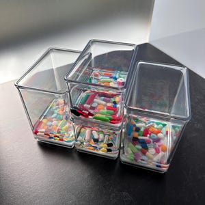 May include: Four clear plastic containers stacked on top of each other, each filled with a variety of colorful pills and capsules.