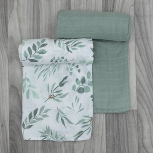 May include: Two muslin swaddles, one with a green solid color and the other with a white background and a green leafy pattern.