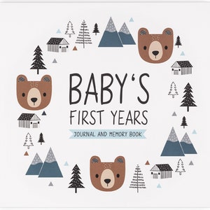 May include: A white baby journal with a brown bear illustration and the text "BABY'S FIRST YEARS JOURNAL AND MEMORY BOOK". The cover features a woodland theme with trees, mountains, and houses.