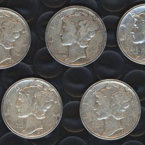 May include: Five silver Mercury dimes, each displaying a profile of a woman with a winged cap. The coins are arranged on a dark, textured surface. Dates visible on the coins include 1939, 1941, 1943, and 1944. These vintage coins are a part of numismatic history.