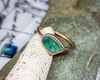 May include: A gold ring with a green opal gemstone. The opal has a teardrop shape and is set in a simple band.