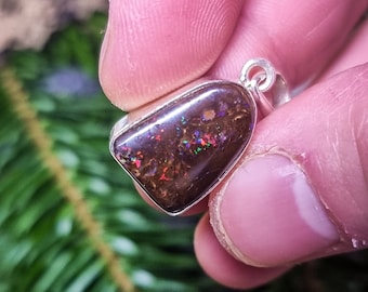 May include: A silver pendant with a dark brown opal stone. The opal has a shimmery, iridescent quality with flashes of red, green, and blue.