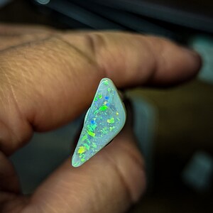 Puede incluir: Una pieza triangular de &oacute;palo blanco con destellos iridiscentes verdes y azules.