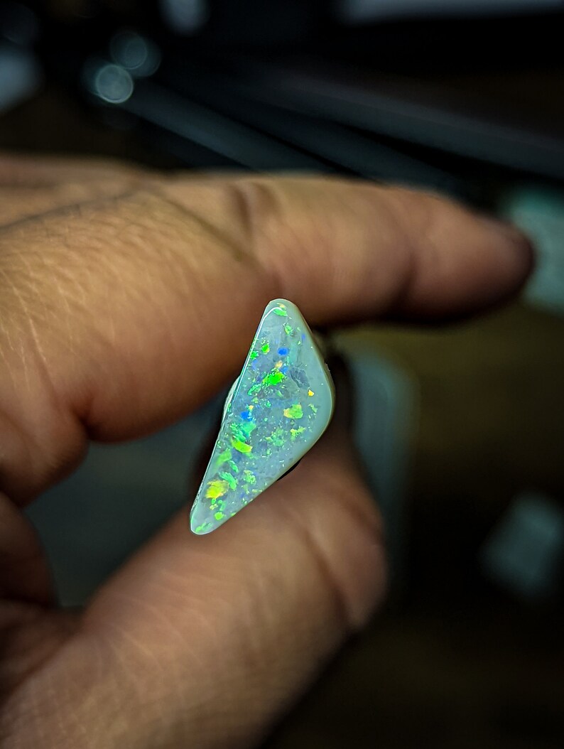 Puede incluir: Una pieza triangular de &oacute;palo blanco con destellos iridiscentes verdes y azules.