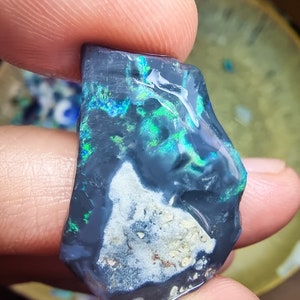 Può includere: Un opale grigio scuro con bagliori verdi e blu. L'opale ha una matrice bianca e grigia.