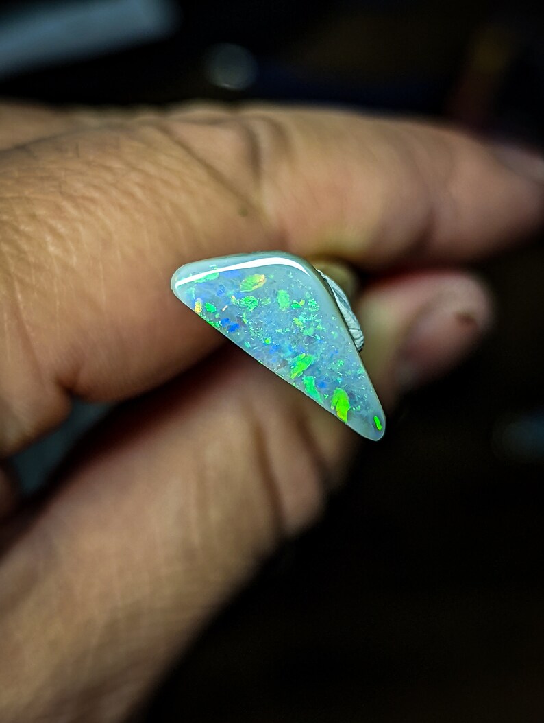 Puede incluir: Una pieza triangular de &oacute;palo con una base blanca y destellos iridiscentes verdes y azules.