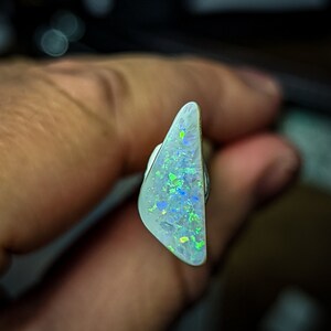 Puede incluir: Una pieza triangular de &oacute;palo blanco con destellos iridiscentes verdes y azules.