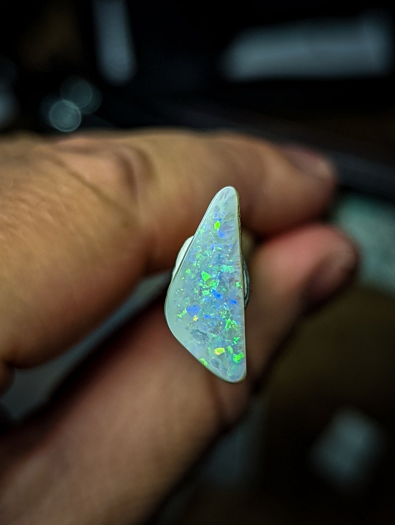Puede incluir: Una pieza triangular de &oacute;palo blanco con destellos iridiscentes verdes y azules.
