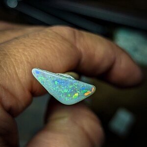 Puede incluir: Una pieza triangular de &oacute;palo con una base blanca y destellos iridiscentes verdes, azules y naranjas.