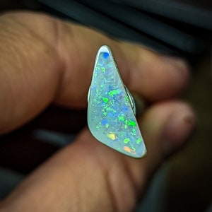 Puede incluir: Una pieza triangular de &oacute;palo con una base blanca y destellos iridiscentes verdes, azules y naranjas.