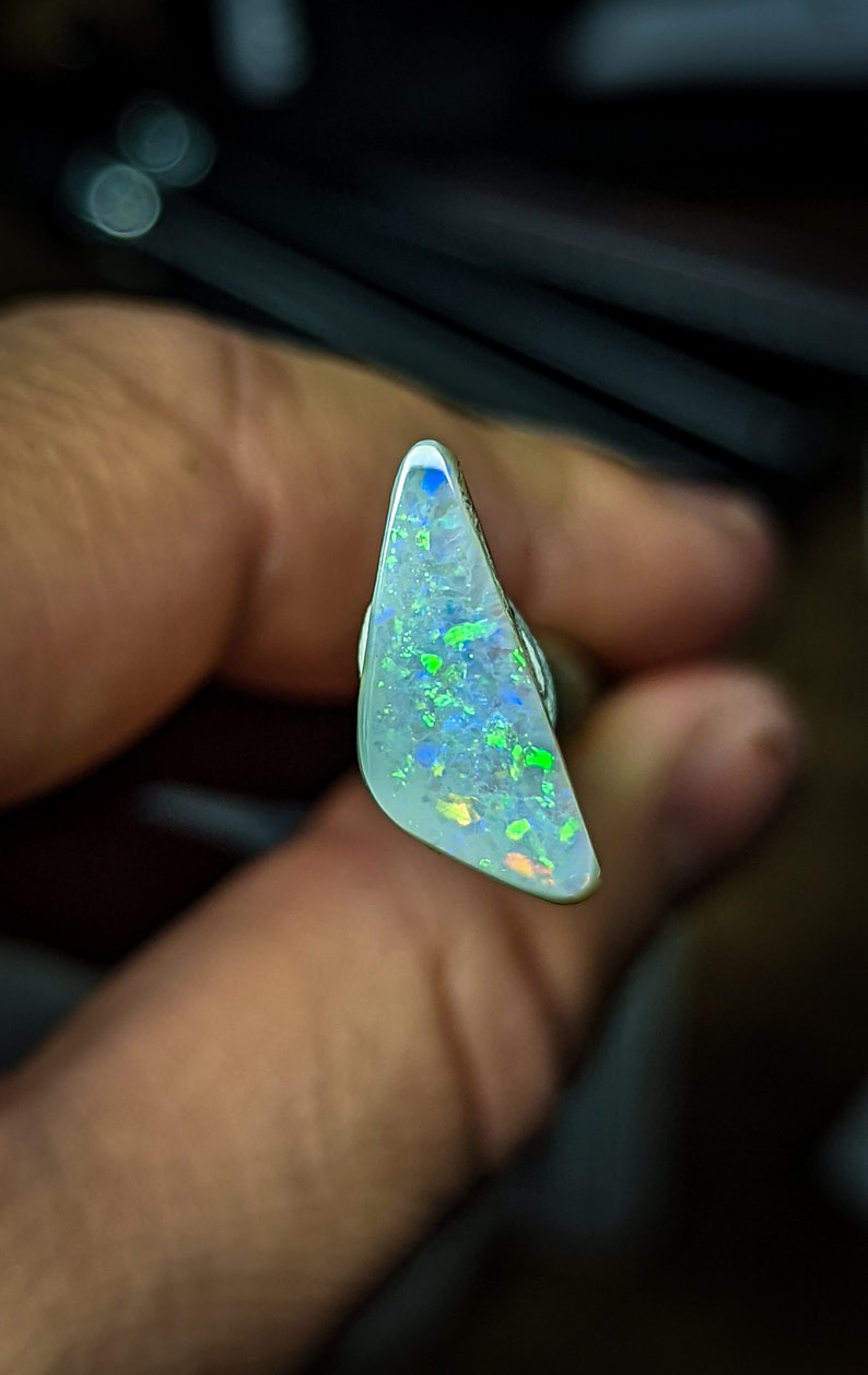 Puede incluir: Una pieza triangular de &oacute;palo con una base blanca y destellos iridiscentes verdes, azules y naranjas.