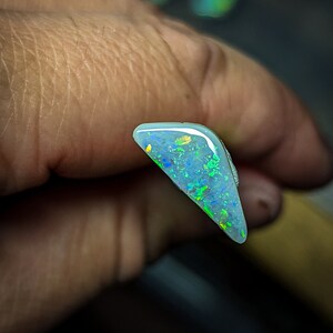 Puede incluir: Una pieza triangular de &oacute;palo con una base azul claro y destellos iridiscentes verdes y amarillos.