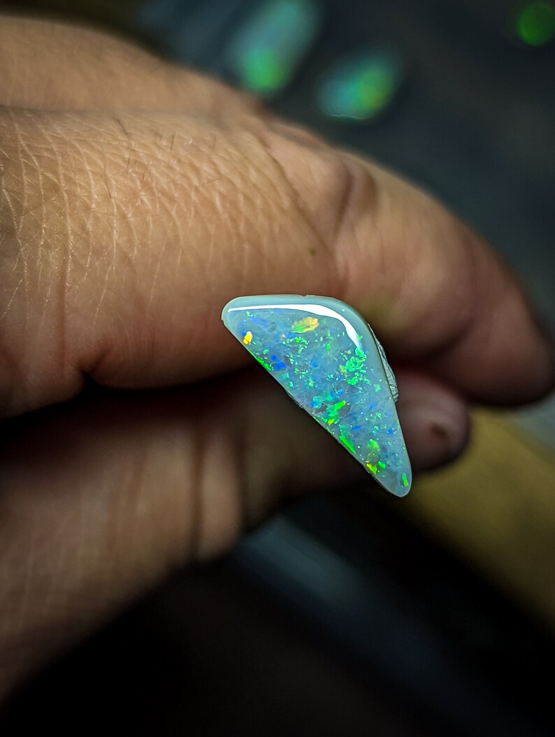 Puede incluir: Una pieza triangular de &oacute;palo con una base azul claro y destellos iridiscentes verdes y amarillos.