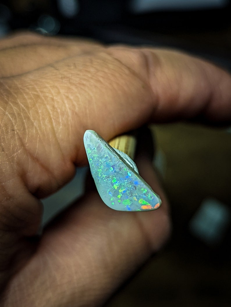 Puede incluir: Una pieza triangular de &oacute;palo blanco con destellos iridiscentes verdes, azules y naranjas.