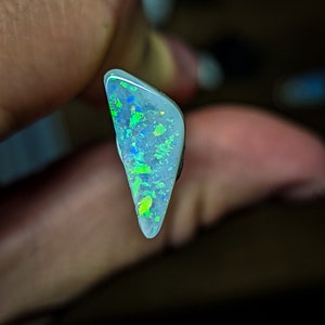 Puede incluir: Una pieza triangular de &oacute;palo con una base blanca y destellos iridiscentes verdes y azules.