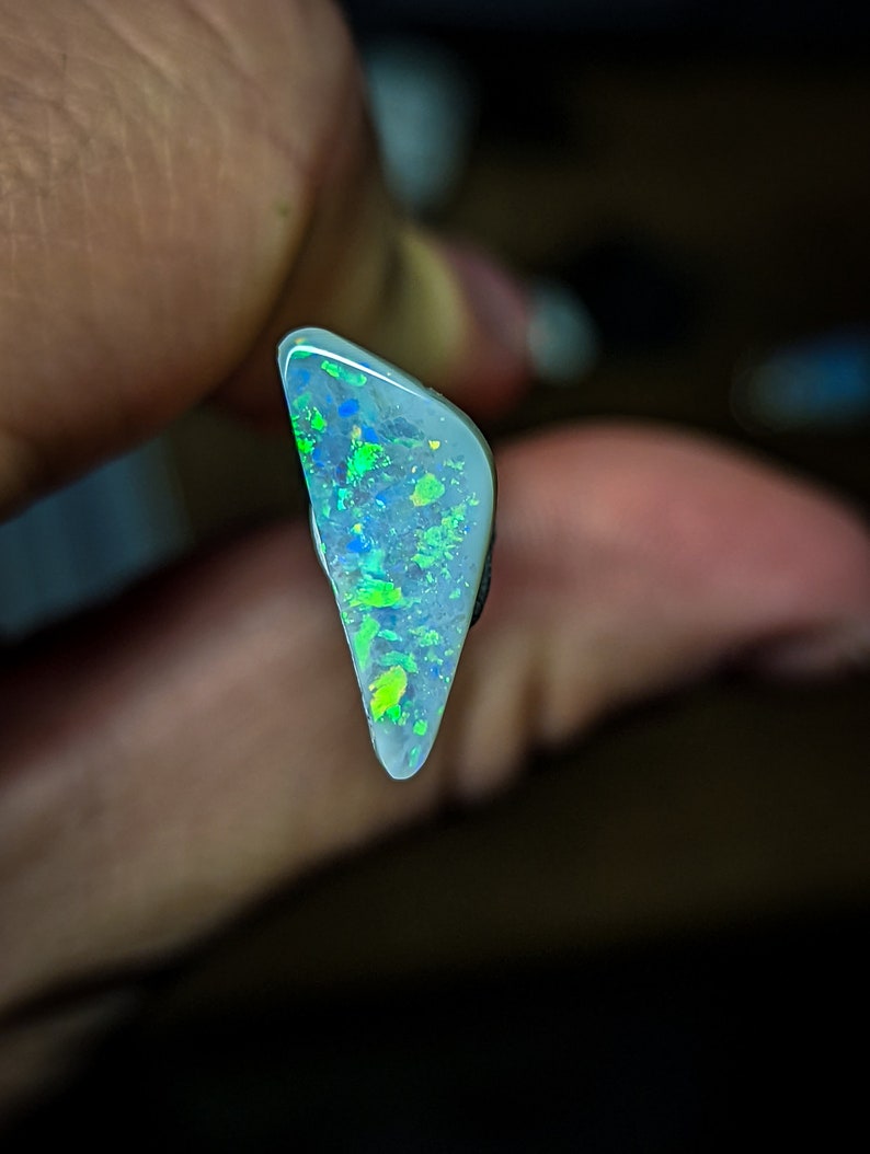 Puede incluir: Una pieza triangular de &oacute;palo con una base blanca y destellos iridiscentes verdes y azules.