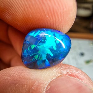 Pode incluir: Uma gema de opala azul e verde com uma forma redonda e lisa. A opala é uma gema natural com um brilho iridescente único.
