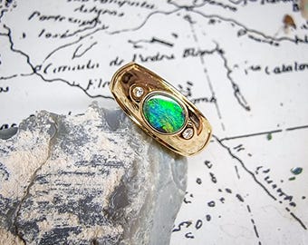 May include: A gold ring with an oval, iridescent green gemstone and two small, clear accent stones. The ring is set on a light gray rock against a backdrop of a vintage map.