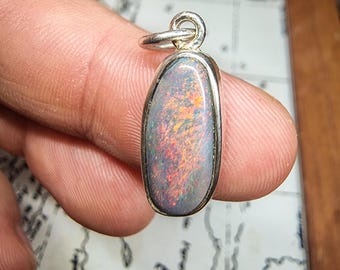 May include: A silver pendant with an oval-shaped opal gemstone. The opal displays a vibrant array of colors, including red, orange, and blue, set within a silver bezel. The pendant has a small loop for a chain.