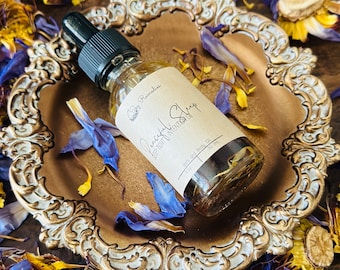 May include: A glass bottle with a dropper top filled with a golden liquid. The bottle is labeled "Peaceful Sleep Essential Oil" and "Body Remedies". The bottle is sitting on a gold-colored decorative tray with a floral design. The tray is surrounded by dried flower petals in shades of blue and yellow.