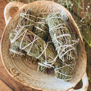 May include: A bowl filled with bundles of dried sage, tied with twine. The sage is a light green color and the bowl is a light brown color.