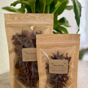May include: Two brown paper bags with clear plastic windows containing star anise. The bags are labeled "Star Anise" and include the text "Jasminum Officinale" and "Organic".