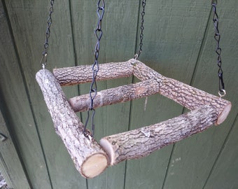 May include: A hanging bird feeder made from natural branches, with a square shape and four sides. The feeder is suspended by two black chains with hooks at the top.