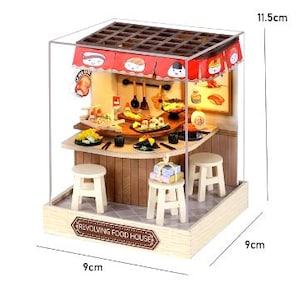 Peut inclure: Une maison de poup&eacute;e de restaurant de sushis en bois miniature avec un coffret en acrylique transparent. La maison de poup&eacute;e comprend un bar &agrave; sushis rotatif, des tabourets et une vari&eacute;t&eacute; de pi&egrave;ces de sushis. La maison de poup&eacute;e mesure 9 cm de large, 9 cm de profondeur et 11,5 cm de haut.