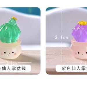 Może przedstawiać: Dwie miniaturowe figurki kaktus&oacute;w w małych doniczkach z uśmiechniętymi buźkami. Zielony kaktus ma 3,5 cm wysokości i 2,1 cm szerokości. Fioletowy kaktus ma 3,1 cm wysokości i 2,1 cm szerokości. Oba mają mały ż&oacute;łty kwiatek na szczycie.