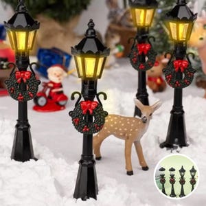 May include: Set of five black miniature streetlights with a warm white LED light and a red and green Christmas wreath. The lights are on a snowy surface with a small deer figurine.