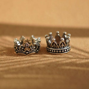 May include: Two silver crown rings with intricate details. The crowns have a pointed top and a beaded edge.