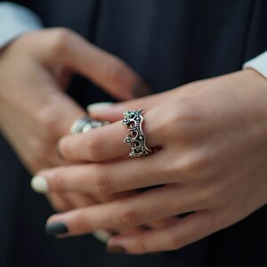 May include: A silver crown ring with intricate details. The ring is worn on a person's finger.