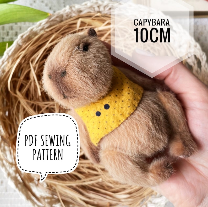 K&ouml;nnte beinhalten: Ein kuscheliges Capybara-Spielzeug, etwa 10 cm lang, mit einer gelben Weste mit Punkten. Das Bild enth&auml;lt den Text "CAPYBARA 10CM" und "PDF SEWING PATTERN". Das Spielzeug liegt in einem geflochtenen Korb.