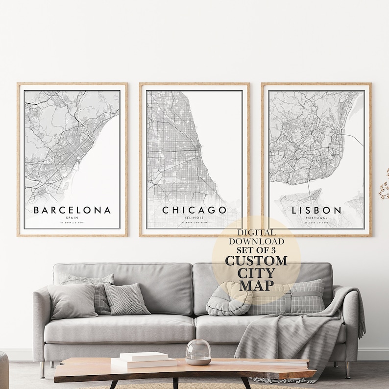 May include: Set of three black and white city maps with the names "Barcelona, Spain", "Chicago, Illinois", and "Lisbon, Portugal" printed below each map. The maps are framed in a light wood frame and are hanging on a white wall. The text "Digital Download Set of 3 Custom City Map" is printed below the maps.