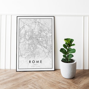 May include: Black and white map print of Rome, Italy, in a black frame. The map shows the city streets and landmarks. The print is hanging on a white wall next to a potted plant.