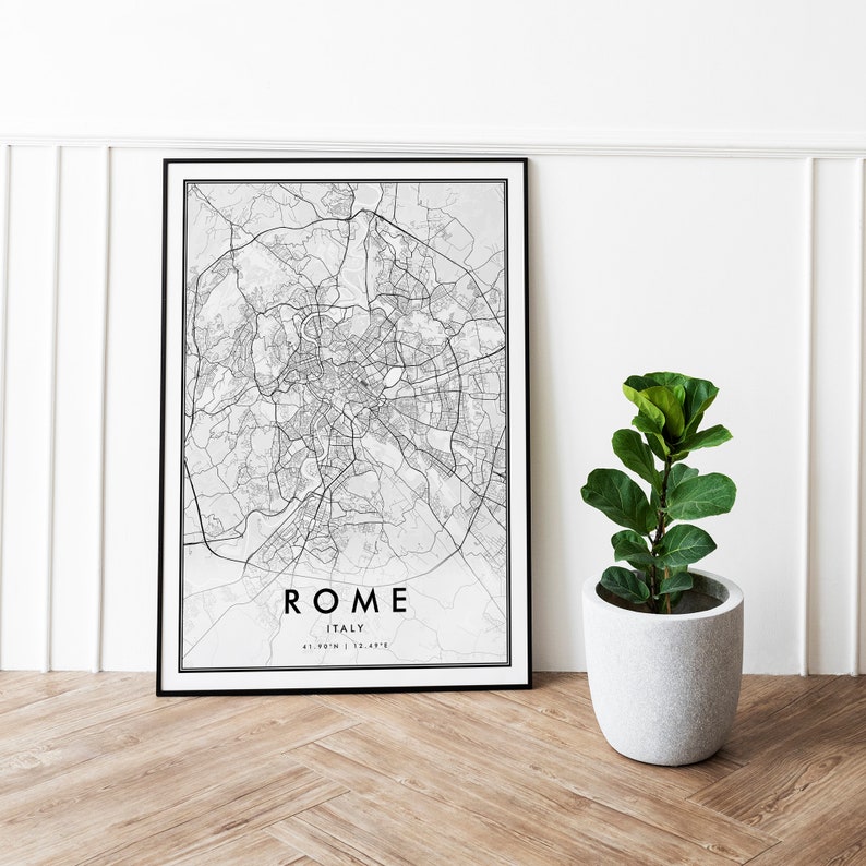 May include: Black and white map print of Rome, Italy, in a black frame. The map shows the city streets and landmarks. The print is hanging on a white wall next to a potted plant.