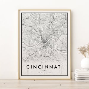 Puede incluir: Una impresión de mapa en blanco y negro de Cincinnati, Ohio con el nombre de la ciudad y las coordenadas impresas en la parte inferior. El mapa está enmarcado en un marco dorado.