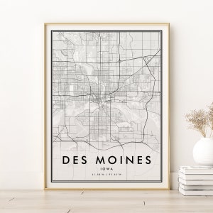 May include: A black and white map print of Des Moines, Iowa. The map shows the city's streets and landmarks. The text "Des Moines, Iowa, 41.58°N | 93.62°W" is printed below the map.