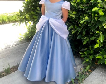 May include: A light blue princess dress with a white bow and puffed sleeves. The dress is made of satin and has a full skirt.