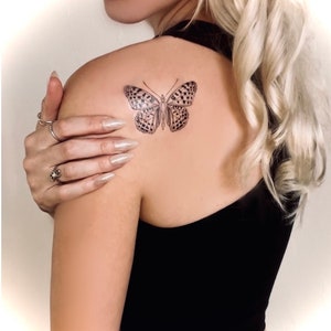 May include: A black and white butterfly tattoo on a person's shoulder.