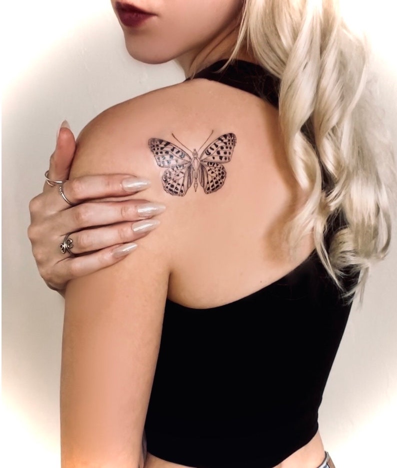 May include: A black and white butterfly tattoo on a person's shoulder.