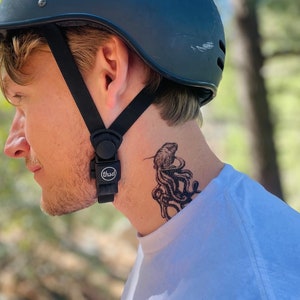 May include: A person wearing a black helmet with a black strap and a white t-shirt. The person has a temporary tattoo of an octopus on their neck.