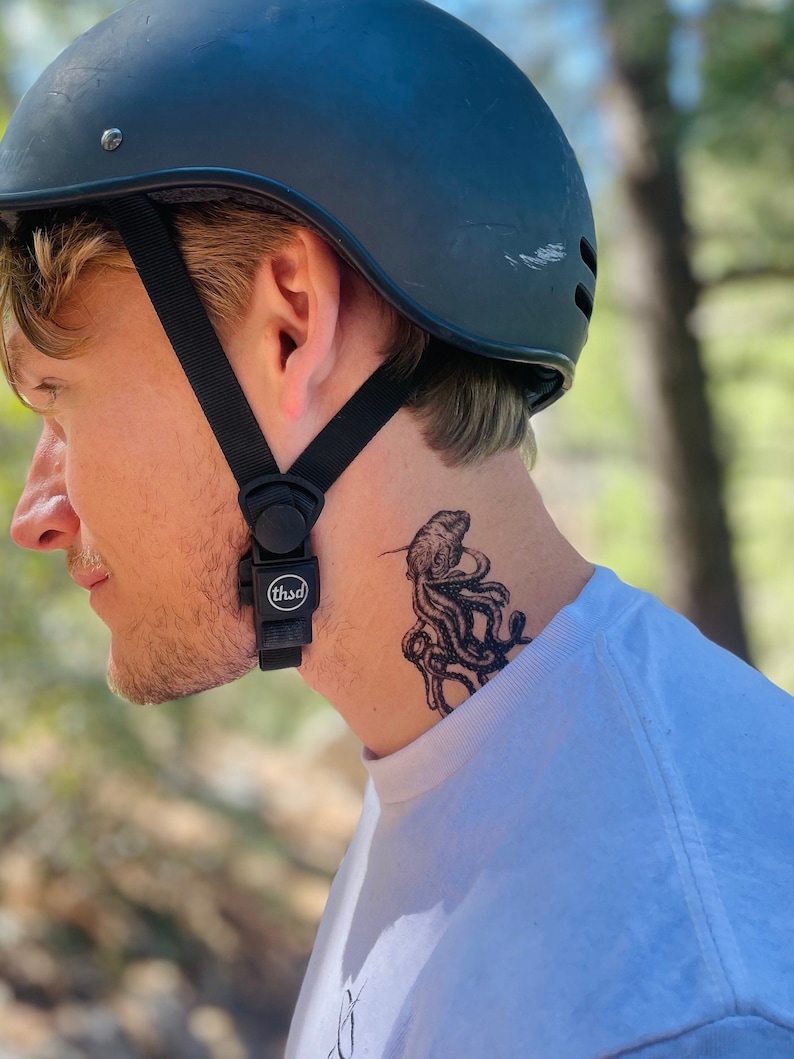 May include: A person wearing a black helmet with a black strap and a white t-shirt. The person has a temporary tattoo of an octopus on their neck.