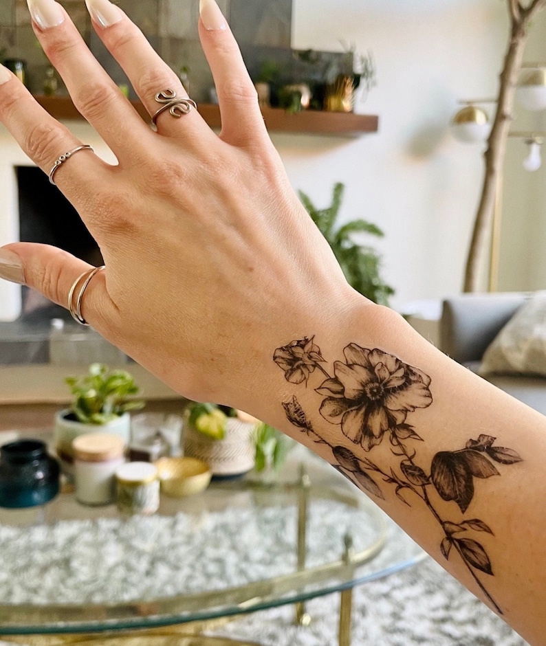 May include: A black and white temporary tattoo of a floral design with three flowers and leaves on a person's wrist.