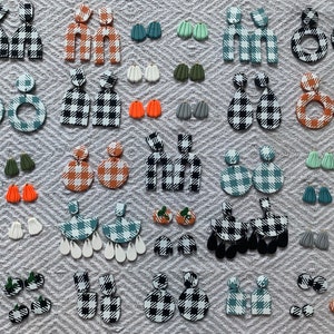 May include: A collection of handmade polymer clay earrings in various shapes and colors, including black and white gingham, orange, green, and blue. The earrings are displayed on a gray textured surface.