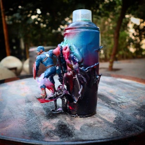 May include: A blue and red spray paint can with a superhero action figure standing on top of it. The can is covered in drips and splatters of paint.